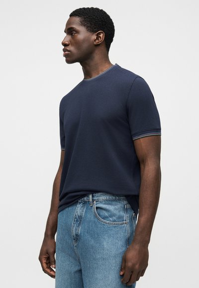 Κοντομάνικο μπλουζάκι σε ναυτικό μπλε χρώμα με στρογγυλή λαιμόκοψη, με διακριτική τρέσα με ρίγες σε χρώματα του ουράνιου τόξου στο λαιμό και τις μανσέτες. Υλικό από βαμβάκι.