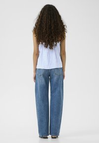 Pasiasty top bez rękawów w niebiesko-białe paski, zestawiony z szerokimi niebieskimi dżinsami. Tkanina wydaje się casualowa, ma luźny krój i brak widocznych akcentów.