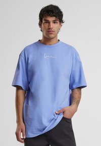Light blue oversized t-shirt made of cotton, featuring short sleeves and a round neckline. White signature logo on the front, smooth texture.