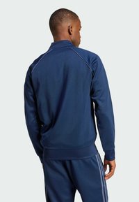 Navy blue athletic jacket featuring a high collar, smooth texture, and contrasting light blue stitching along the shoulders.