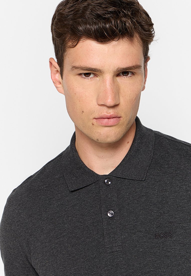 Polo shirt gris anthracite avec un col classique, deux boutons et un logo brodé discret sur la poitrine. Tissu doux et texturé.