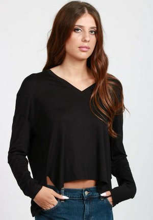 Maglietta nera a maniche lunghe e taglio corto con scollatura a V, caratterizzata da una vestibilità ampia e orlo grezzo. Abbinata a jeans in denim blu a vita alta.