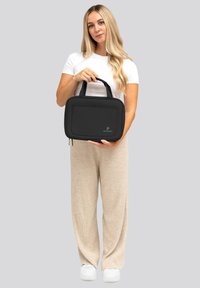 Borsa in tessuto nero con struttura imbottita, chiusura con zip e due manici; presenta un pannello frontale con logo.
