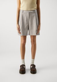 Shorts gris ajustés avec plis sur les côtés et texture lisse, associés à des chaussures Mary Jane marron et des chaussettes légères.