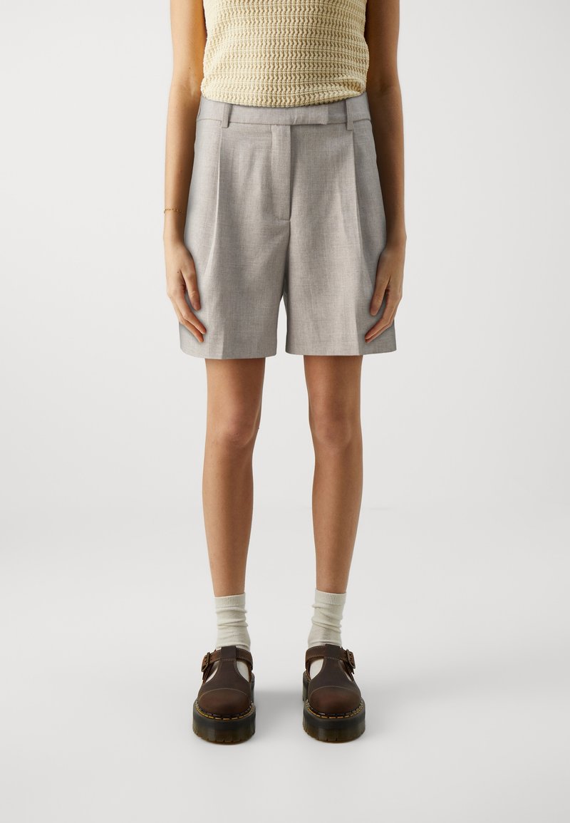 Shorts gris ajustés avec plis sur les côtés et texture lisse, associés à des chaussures Mary Jane marron et des chaussettes légères.