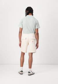 Kortærmet, lysegrønt tekstureret skjorte parret med cremenfarvede, knælange shorts med to baglommer og elastisk talje.