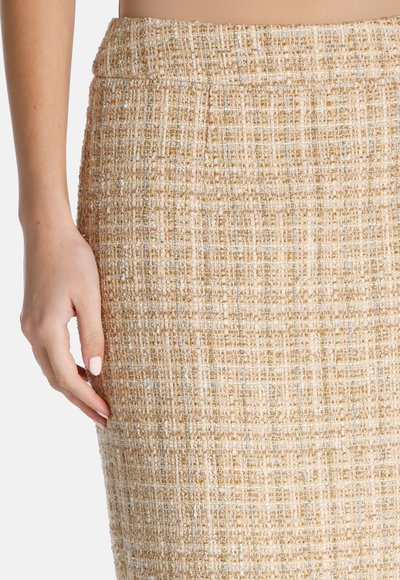 Polviin ulottuva vaaleanbeige tweed-hame, jossa on teksturoitu kuvio, joka sisältää kultaisia ja hopeisia säikeitä. Vyötärö on sileä ja tiukka.