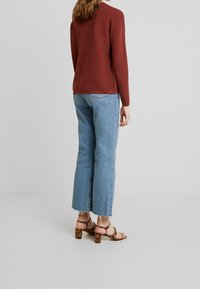 Pull côtelé bordeaux, jean droit bleu clair avec ourlet brut, et sandales marron à imprimé léopard avec talons carrés.