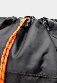 Sac à cordon en nylon noir avec cordon orange contrastant, doté d'une fermeture à bascule en plastique et d'une finition de surface texturée.