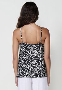 Débardeur sans manches à motifs de feuilles noir et blanc avec des bretelles fines, offrant une coupe décontractée et un tissu texturé. Le design à l'arrière est simple et épuré.