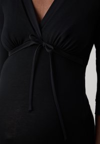 Zwarte wikkeljurk met lange mouwen, voorzien van een gestrikt taille en geplooide stof bij de buste. Glad textuur en aansluitende pasvorm rond de torso.