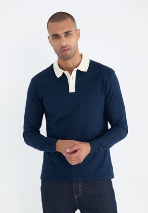 Marineblauw poloshirt met lange mouwen en een crèmekleurige kraag, placket met twee knopen en geribbelde manchetten. Gemaakt van katoen, ontspannen pasvorm, minimalistisch ontwerp.