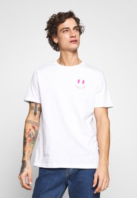 White cotton t-shirt featuring a pink smiley face graphic on the chest. Classic fit with a round neckline and short sleeves.