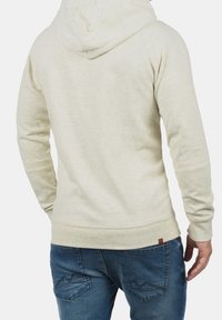 Jasno beżowy hoodie o teksturowanym wykończeniu, z kapturem i ściągaczami przy rękawach. Połączony z niebieskimi dżinsami z akcentami kieszeni.