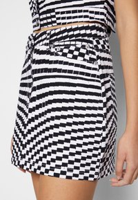 Svartvit mönstrad kjol i bomull med rutmönster, framfickor och metallaccenter vid midjan.