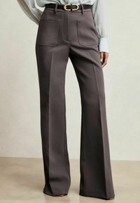 Pantaloni a gamba larga su misura in tessuto grigio scuro, con tasche frontali e una cintura con fibbia dorata, rifiniti con una texture liscia.