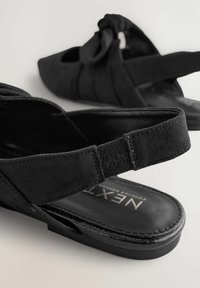 Sandalias de ante negro con diseño de punta abierta, acento de lazo y correa elástica. Presentan una suela plana texturizada y una plantilla acolchada.