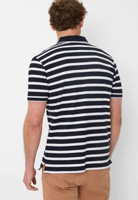 Navy and white striped polo shirt with short sleeves and a collar. Features side slits and a textured fabric. Rear view shown.