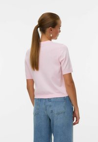 Rosa kortärmad stickad topp med rund halsringning, kombinerad med ljusblå högmidjade denimjeans. Slät textur, avslappnad passform, inga synliga mönster.