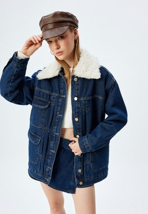 Veste en denim avec un col en fausse peau de mouton blanc, grandes poches avant, quincaillerie dorée et coupe décontractée. Accompagnée d'une casquette brune.