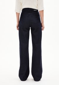 Jeans ampi a vita alta di colore blu scuro, realizzati in denim. Presentano tasche posteriori, un cinturino elastico con marchio e una vestibilità morbida.