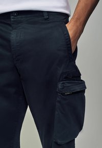 Pantalones cargo en color navy con una textura suave, que cuentan con bolsillos laterales con cremalleras y una cintura ajustada. Elaborados en un tejido ligero y flexible.