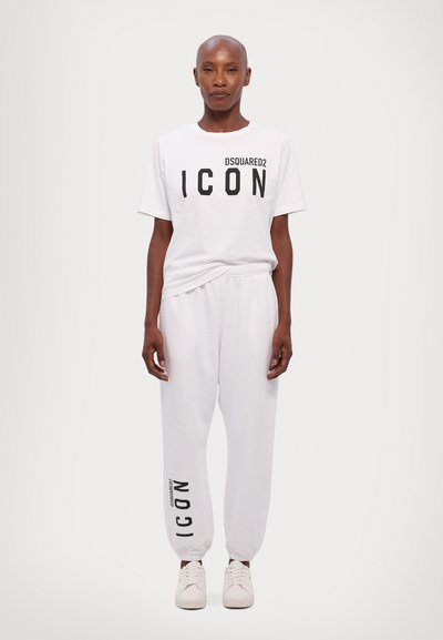 Valkoinen puuvillapaita, jossa on mustat "DSQUARED2 ICON" -tekstit, yhdistetty valkoisiin verkkareihin, joissa on musta "ICON"-kuvio sivussa, ja päällä valkoiset lenkkarit.