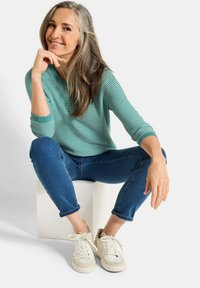 Helles türkis gestreiftes Sweatshirt mit Dreiviertelärmeln, kombiniert mit blauen Jeans und weißen Sneakern. Einfaches, lässiges Design mit gerippten Bündchen.