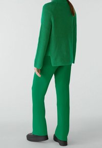 Pull en tricot vert à manches longues et col montant, associé à un pantalon vert assorti, tous deux présentant une texture lisse et une coupe ajustée.