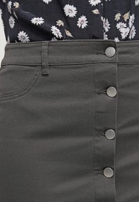 Grå denimkjol med knappstängning fram, prydd med metallknappar och en mjuk textur. Komplett med en blommönstrad topp.