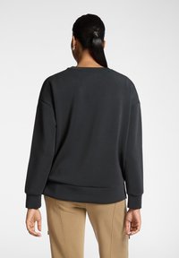 Schwarzer Pullover mit weitem Schnitt, gerippten Bündchen und Saum. Der Stoff wirkt weich und glatt, kombiniert mit beigen Hosen im unteren Bereich.