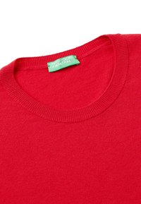 Punainen neulepaita, jossa on pyöreä pääntie ja resorit. Etiketissä lukee "United Colors of Benetton" vihreällä taustalla. Sileä pinta.