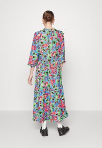 Vestido longo e floral com padrões em vermelho brilhante, verde e preto sobre um fundo azul. Possui cintura franzida e barra rodada.
