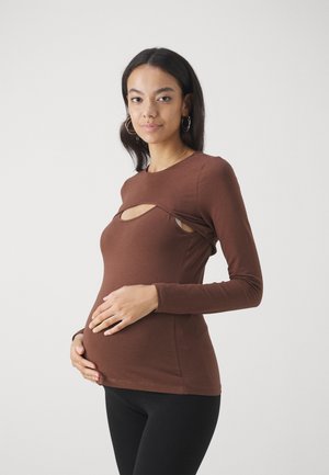 Haut marron à manches longues avec un détail découpé au niveau de la poitrine et une coupe ajustée, fabriqué en tissu doux et extensible. Associé à des leggings noirs.
