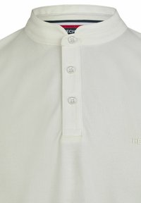 Helles beige Polo-Shirt mit kurzen Ärmeln und Stehkragen, ausgestattet mit drei weißen Knopfverschlüssen und dezenter strukturiertem Stoffdetail.