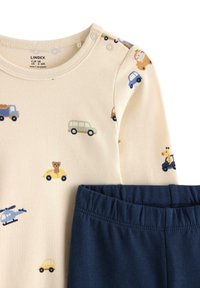 Ensemble de pyjama en coton comprenant une chemise crème ornée d'imprimés de voitures et d'animaux, associée à un pantalon élastique taille noire marine.