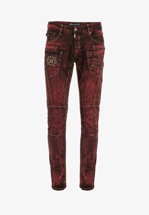 Red denim jeans with a faded, textured finish. Features multiple pockets, decorative stitching, and unique embroidered accents.