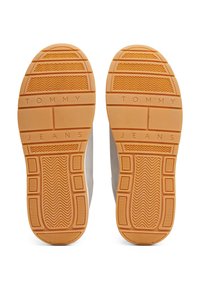 Semelles de chaussures avec une bande de caoutchouc orange, présentant "TOMMY JEANS" embossé au centre et des zones de grip à motifs.