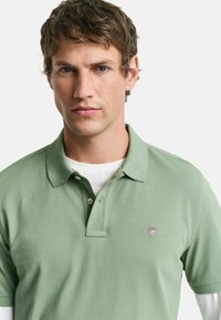 Polo de algodón verde claro, con cuello clásico, tres botones y un pequeño logo bordado en el lado izquierdo del pecho.