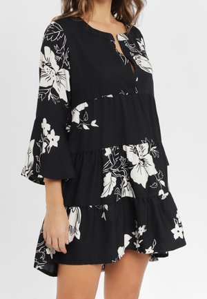 Vestido negro en capas con estampado floral blanco, mangas de campana tres cuartos y escote redondo con una pequeña abertura frontal.