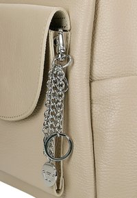 Beżowa skórzana torba z zamkiem błyskawicznym, łańcuszkowymi detalami z metalowymi pierścieniami oraz gładką fakturą na powierzchni.