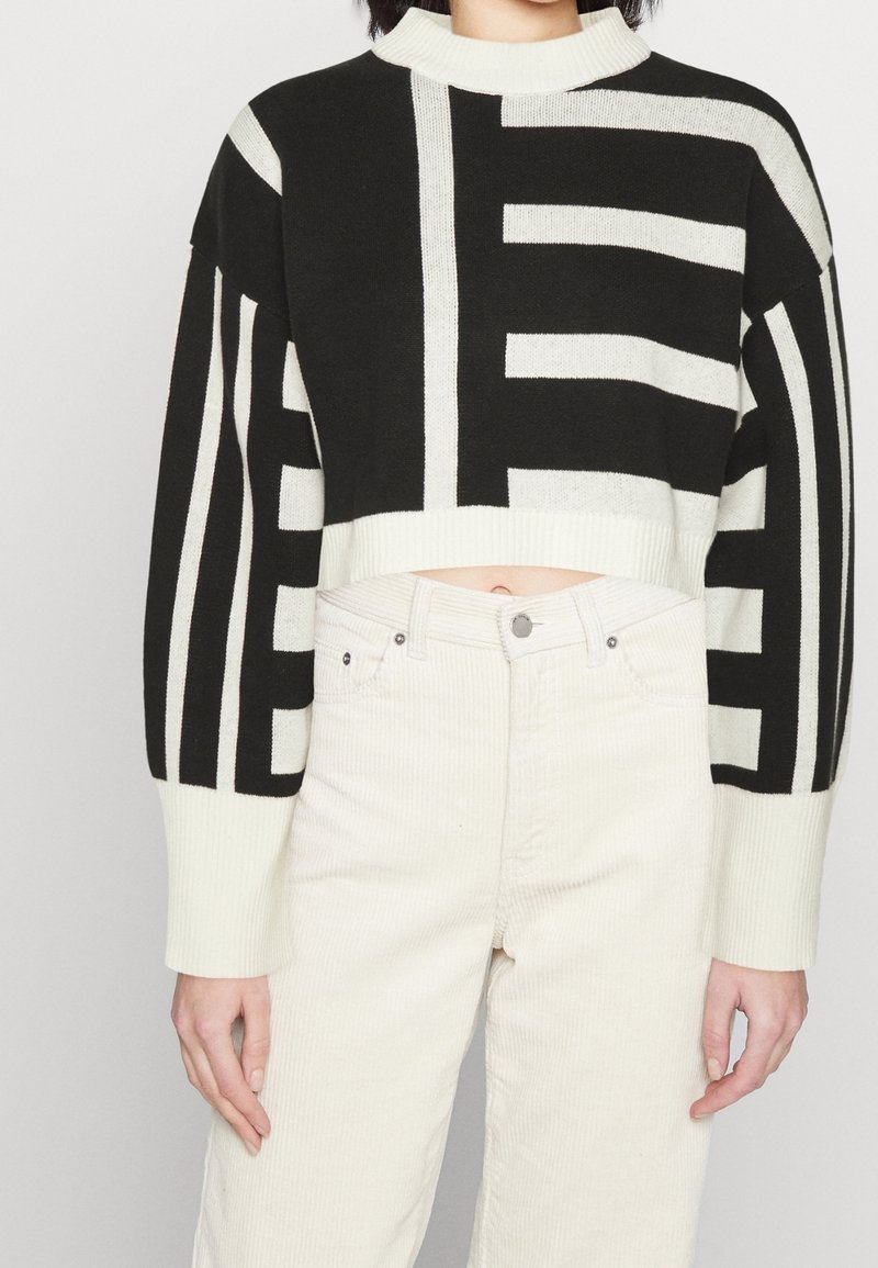 Pull noir et blanc raccourci avec de larges rayures et un col montant, associé à un pantalon en velours côtelé de couleur claire. Matière en maille douce.