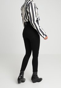 Uppklippt randig skjorta i marinblått och vitt, svarta högmidjade tajta jeans och svarta ankelboots med dragkedjedetalj, sedd bakifrån.