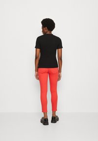 Svart tettsittende t-skjorte med korte ermer, parret med klare røde skinny jeans og svarte klumpete sko, sett bakfra.