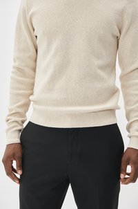 Beige gebreid sweater met een textuurlag, ronde hals en aansluitende boorden, gecombineerd met zwarte broeken van een gladde stof.