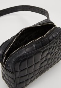 Borsa a tracolla nera in pelle con texture trapuntata, chiusura con zip e interno semplice. Presenta una tracolla sottile e dettagli in metallo argento.