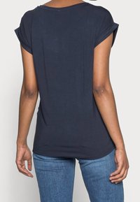 T-shirt a maniche corte blu navy con vestibilità ampia, texture liscia e dettaglio delle maniche arrotolate. Abbinato a jeans azzurri.