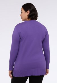 Violetti neulepaita, jossa on pitkät hihat, ribattu helma ja sivuhalkiot, valmistettu pehmeästä neuloksesta. Suunnittelussa on pyöreä kaula-aukko ja olkatyynyt.