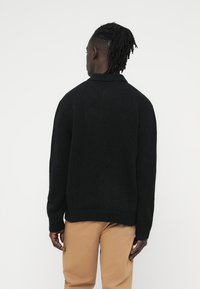 Μαύρ η πλεκτή ζακέτα με ριμπ λαιμόκοψη και τελείωμα, με άνετη εφαρμογή. Η υφή φαίνεται απαλή και ζεστή, κατάλληλη για στρώσεις.