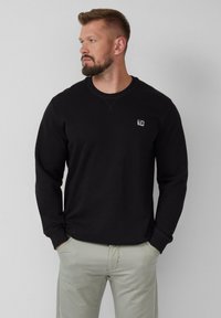 Black crewneck sweatshirt with long sleeves, ribbed cuffs, and a small logo patch on the chest. Made of soft, durable fabric.